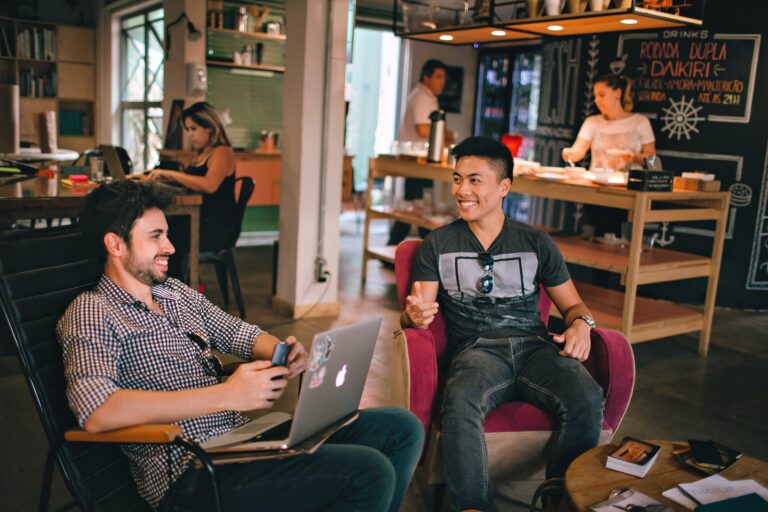 DG Speaks - Travel - The Digital Nomad Networking -Two men smiling and engaged in conversation at a lively co-working space, exemplifying the positive and collaborative atmosphere fostered by shared professional environments.