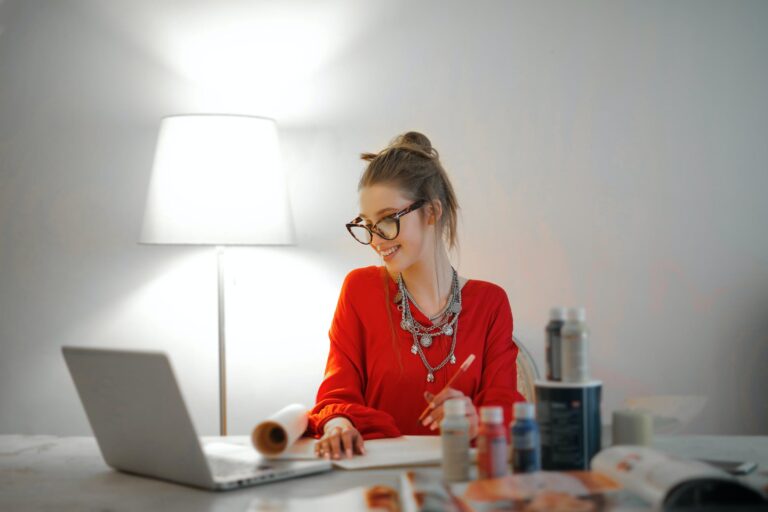 DG Speaks - Travel - Money - Woman in red long sleeve shirt looking at her laptop