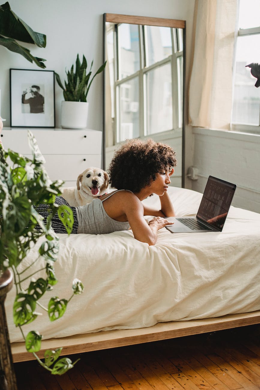 DG Speaks - Travel - Money - Relaxed black woman watching laptop near dog on bed