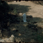 A still from Non/Living, featuring a ghostly figure wandering among ancient ruins with decaying celluloid in the foreground.