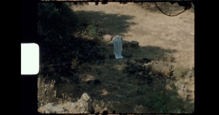 A still from Non/Living, featuring a ghostly figure wandering among ancient ruins with decaying celluloid in the foreground.