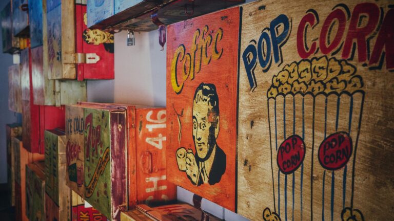 Vintage-style wooden crates featuring colorful retro advertisements for coffee, popcorn, and soda, arranged artistically on a wall showing the relationship between food and pop culture.