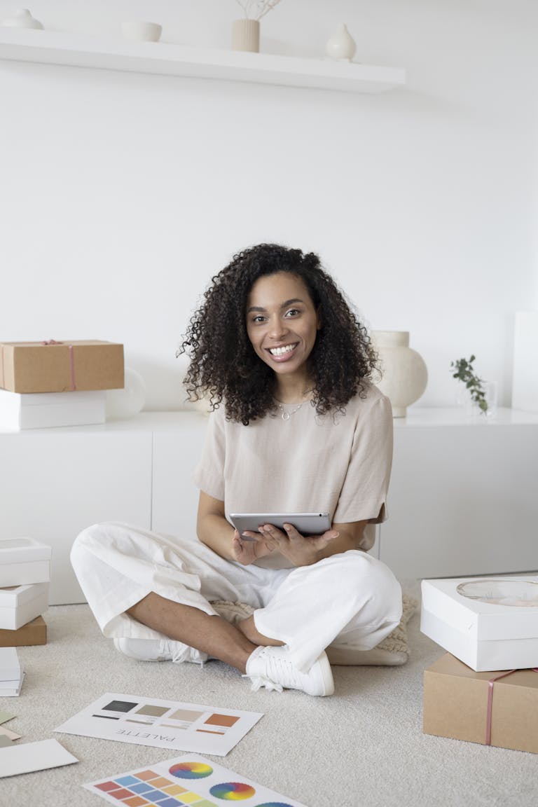 A confident young woman sitting among packages and papers while using a tablet, showcasing modern Amazon entrepreneurship.