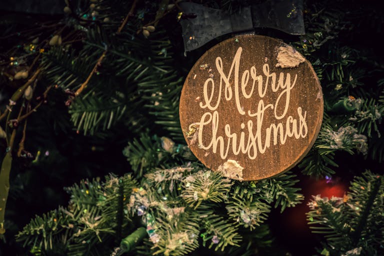 Close-up of a Merry Christmas ornament on a decorated fir tree, evoking festive Christmas Day spirit.