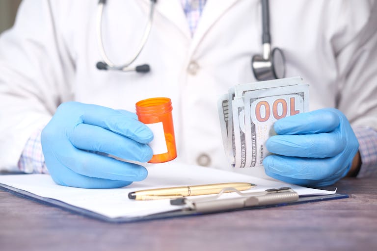 Doctor in gloves holding pill bottle and cash, highlighting medical expenses for story about United Healthcare.