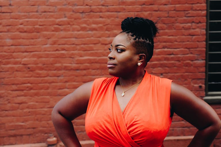 Portrait of a confident woman in a red dress posing against a brick wall representing new opportunities in 2025.