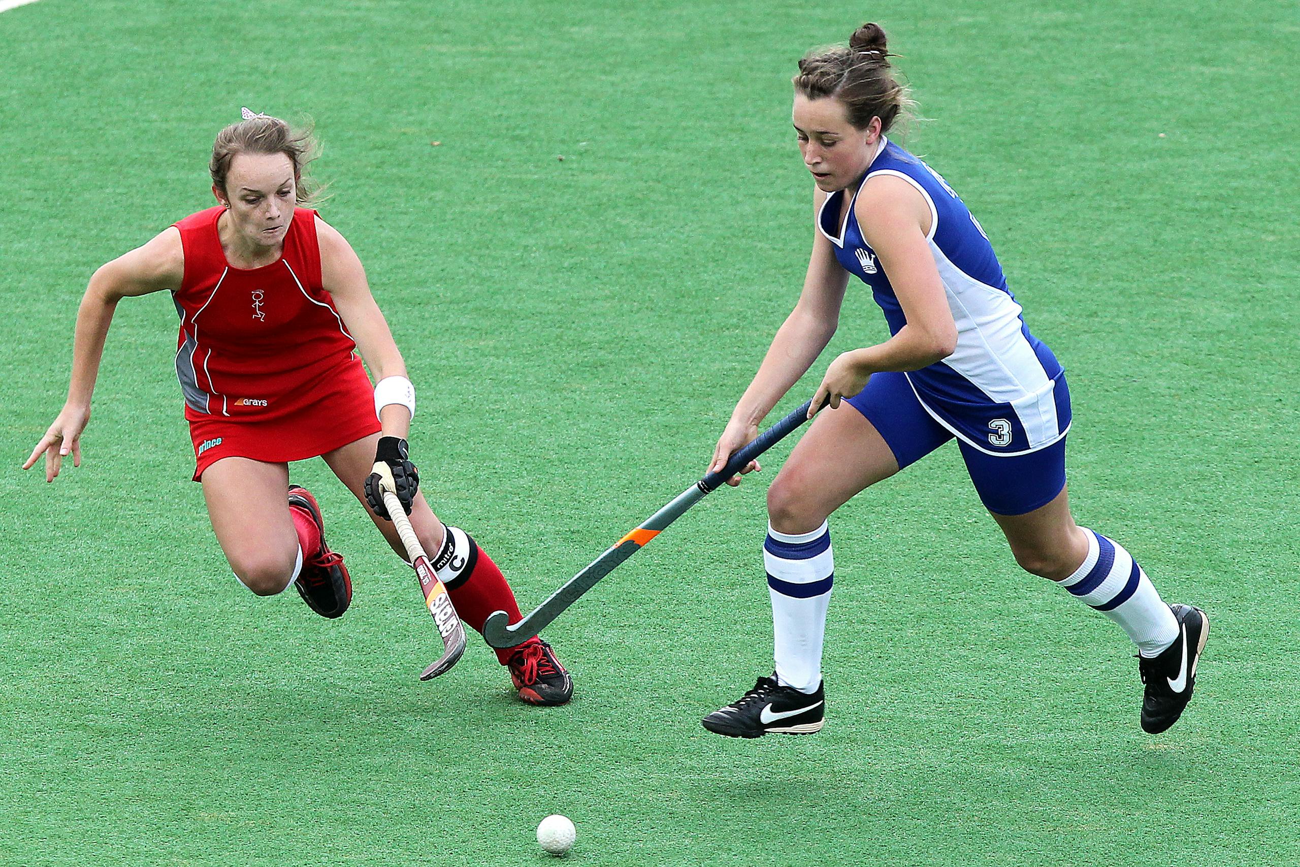 Two female athletes compete in a dynamic field hockey match on a green field for women’s sports.
