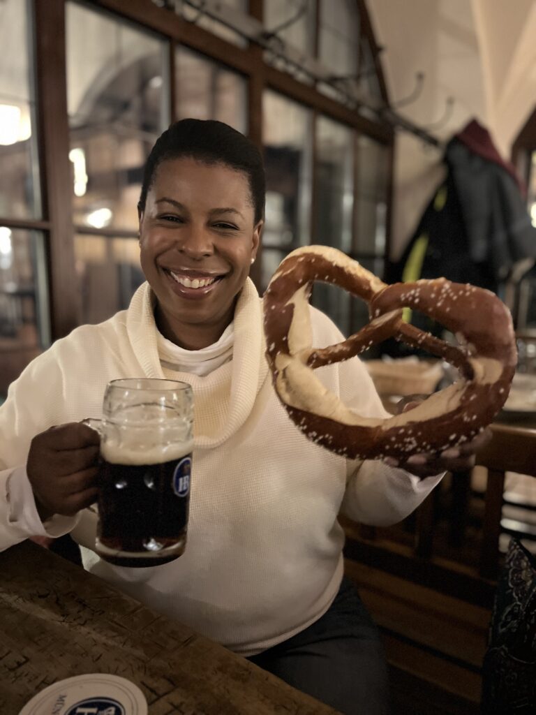 National Pretzel Day - Mercedes at Hofbräuhaus Munich, holding a giant pretzel and pint of beer.