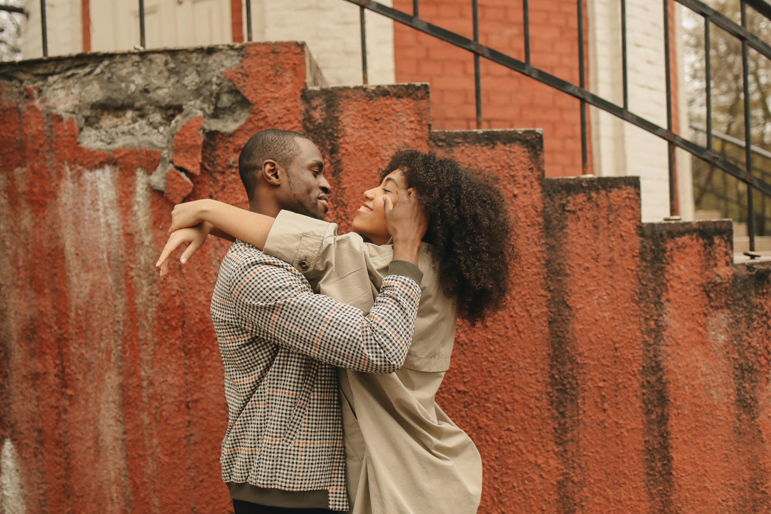 A loving couple sharing a joyful, warm embrace near a rustic staircase outdoors.