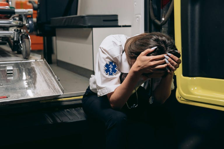 Female trauma. EMT in distress sitting inside an ambulance, head in hands signifying stress and exhaustion.