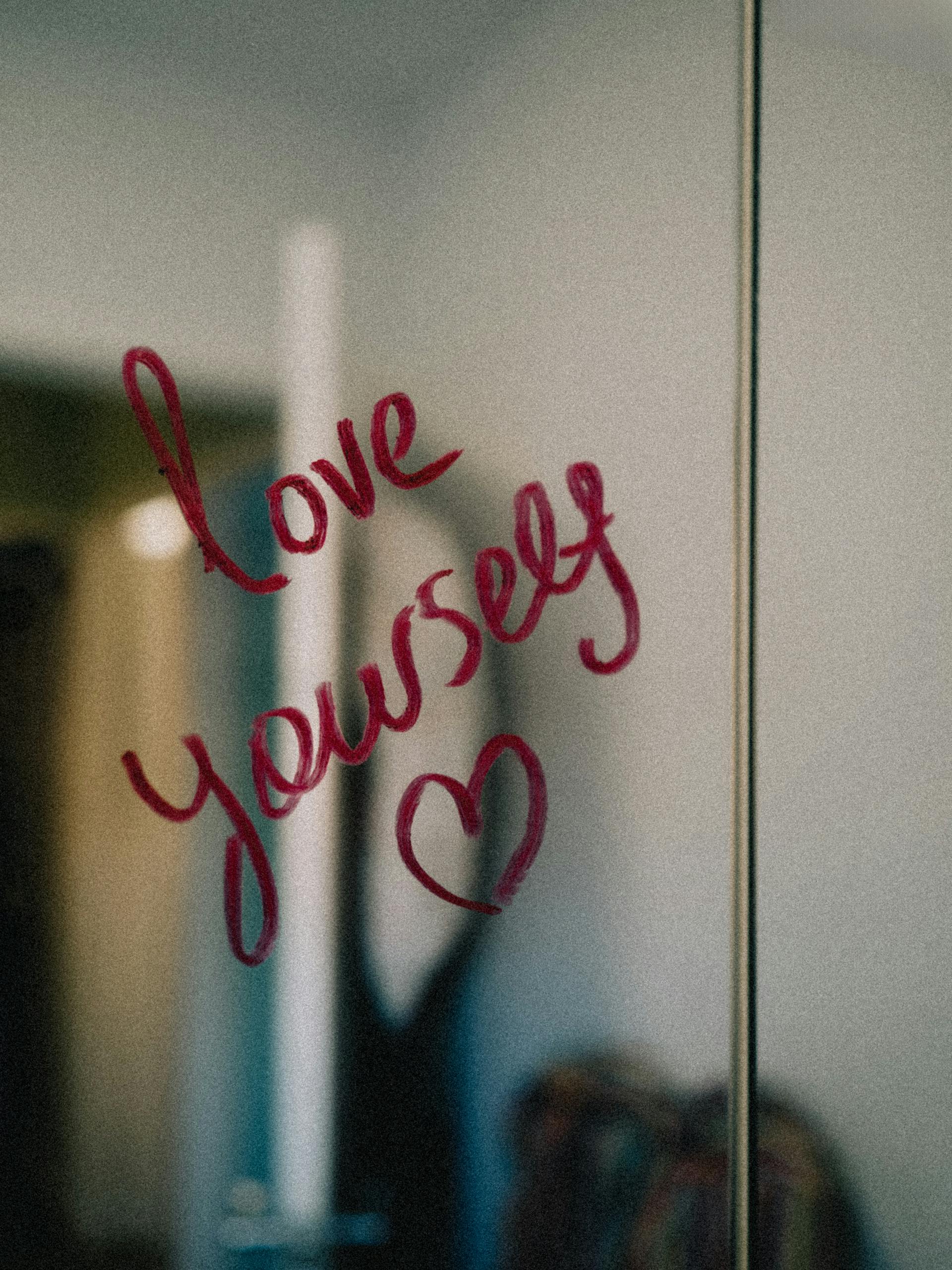Positive affirmation written on a mirror in red lipstick: Love Yourself. Happy Valentine's Day.