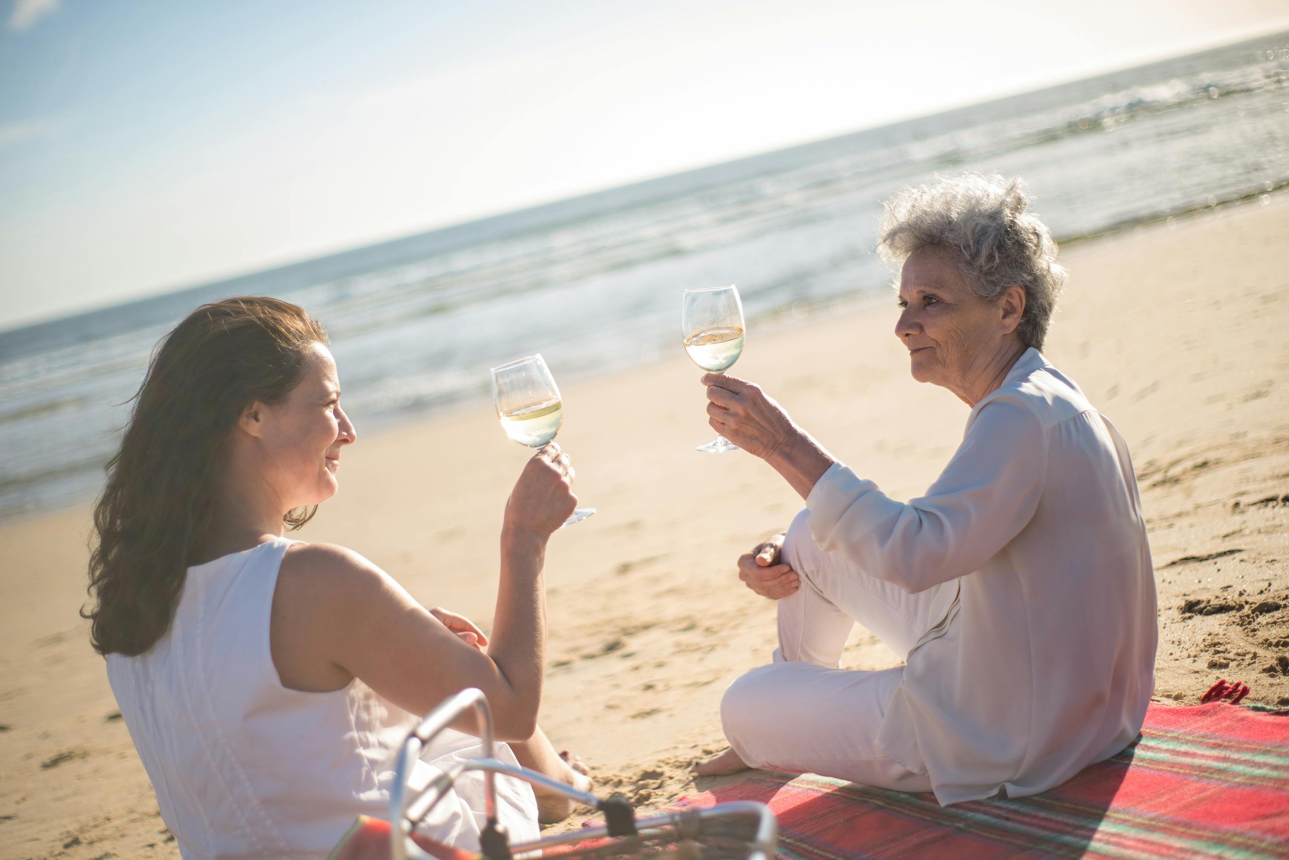 A mother and daughter sharing a joyful moment with wine on a beach in Portugal.