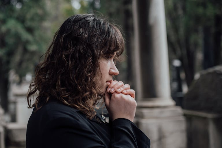 A woman in a cemetery expressing grief and contemplation in a serene outdoor setting.