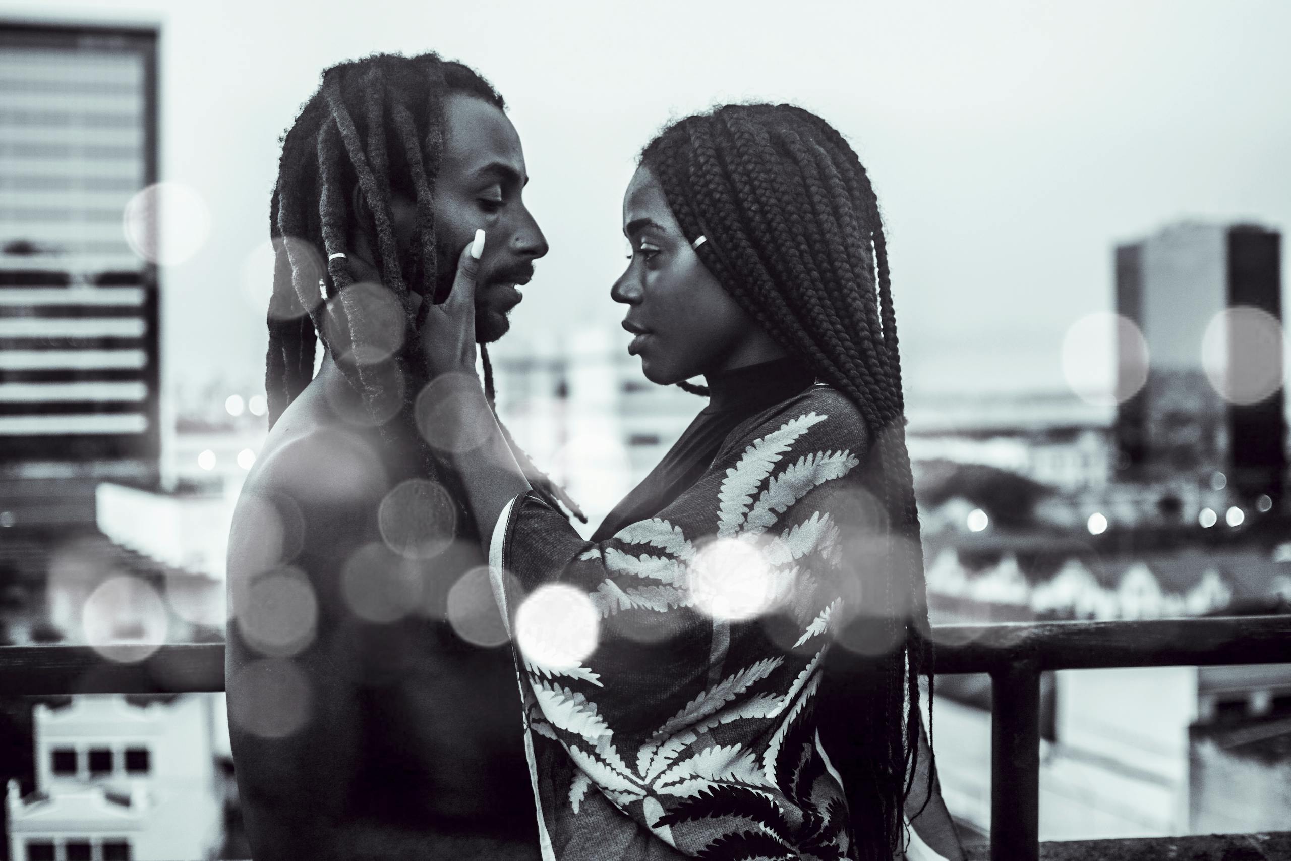 Black leads without Black romantic partners in film - A romantic black and white photo of a couple embracing on a city rooftop with bokeh effect.