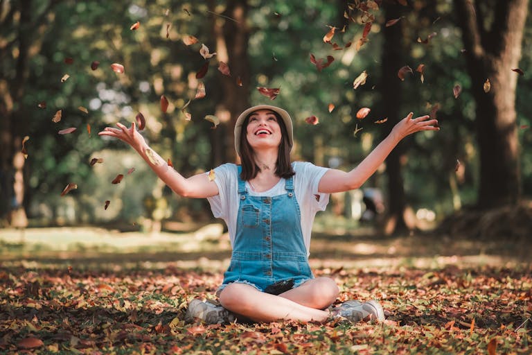 Citizen Kane - Smiling woman in park playfully tossing autumn leaves, enjoying a carefree moment outdoors.