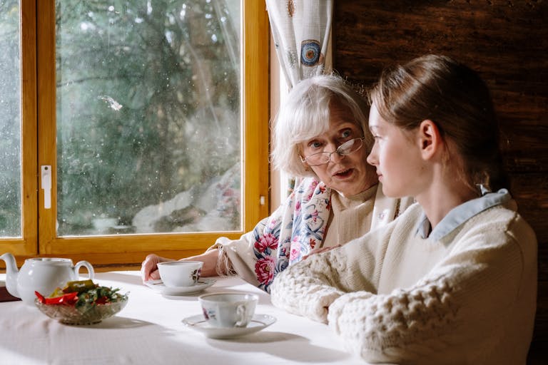 Mother-in-law and bride sharing tea and conversation by a window.