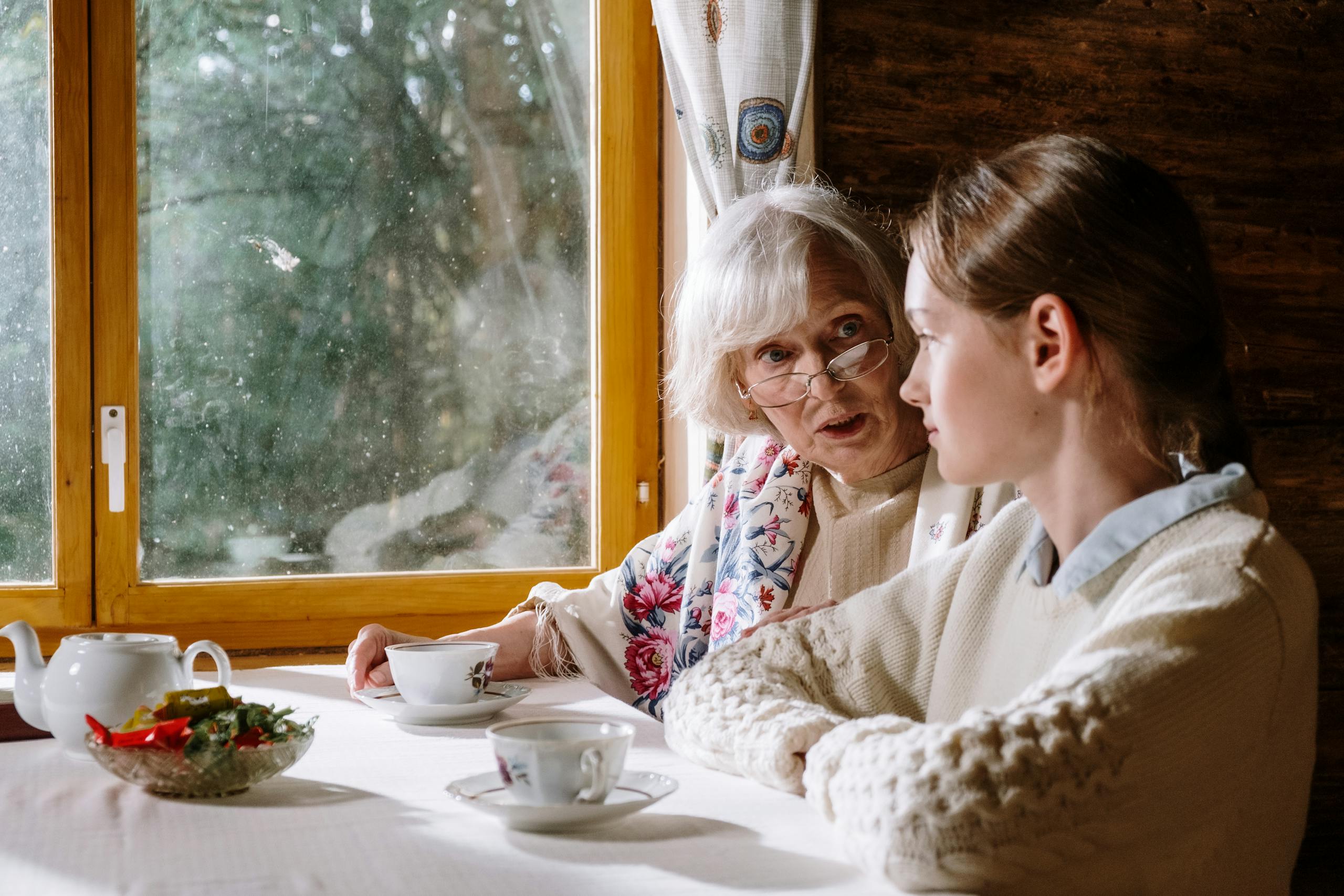 Mother-in-law and bride sharing tea and conversation by a window.