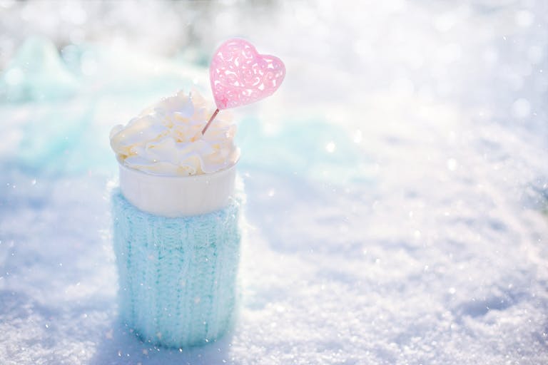 Warm beverage topped with cream in snow, perfect for winter themes.