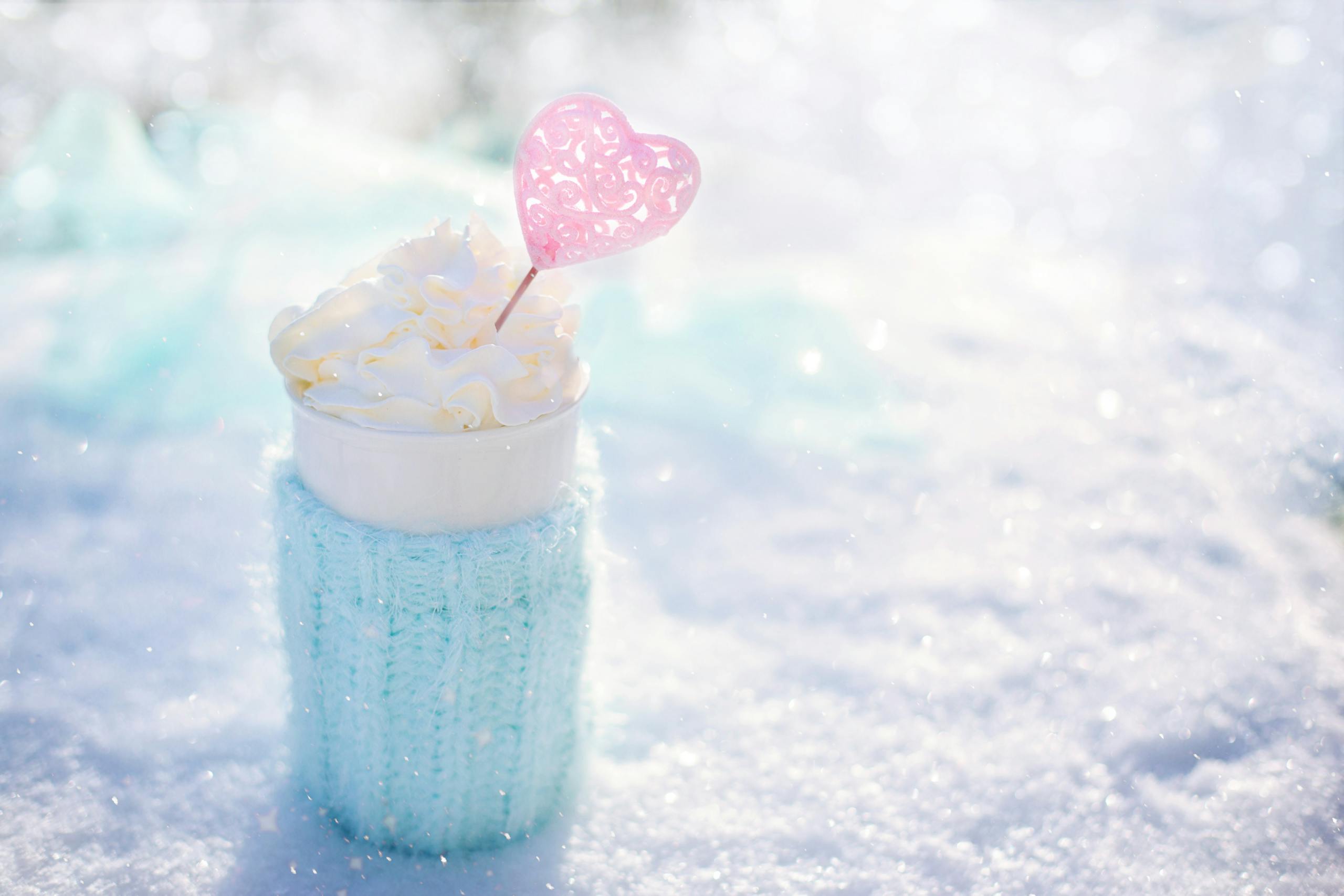 Warm beverage topped with cream in snow, perfect for winter themes.