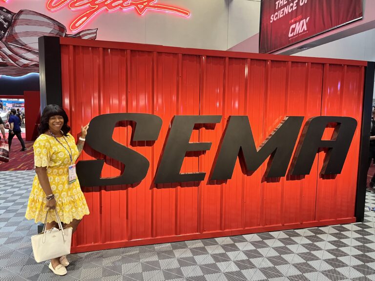 Mercedes at Sema Show in Las Vegas standing next to event sign wearing a yellow dress
