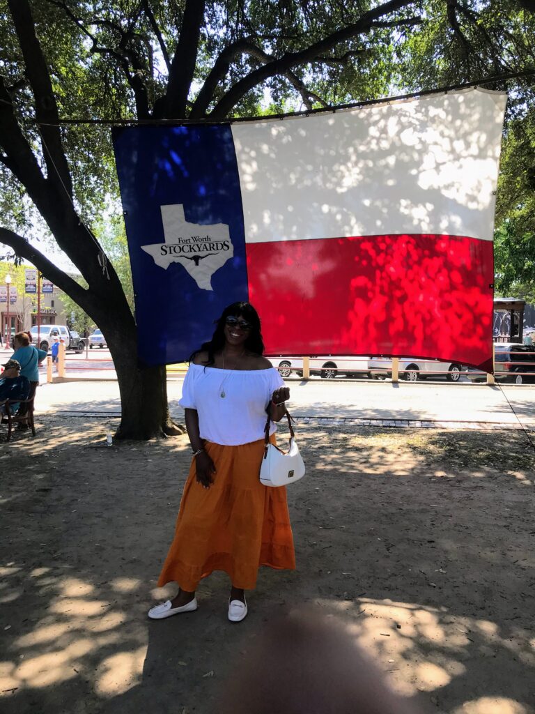 Mercedes Diane Griffin Forbes visiting the Fort Worth Stockyards in Texas beneath the iconic Texas flag.