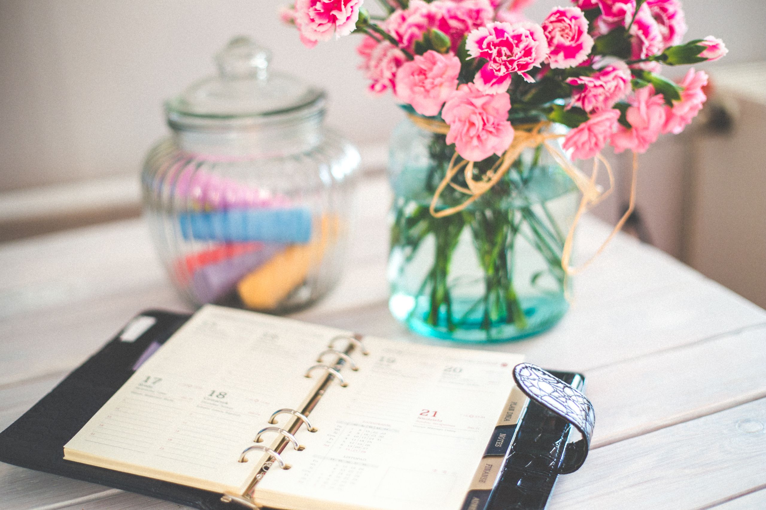 Airbnb Calendar Management: How to Keep Your Booking Calendar Organized and Profitable - A chic desk setup with an open planner and a vase of pink flowers, ideal for productivity.