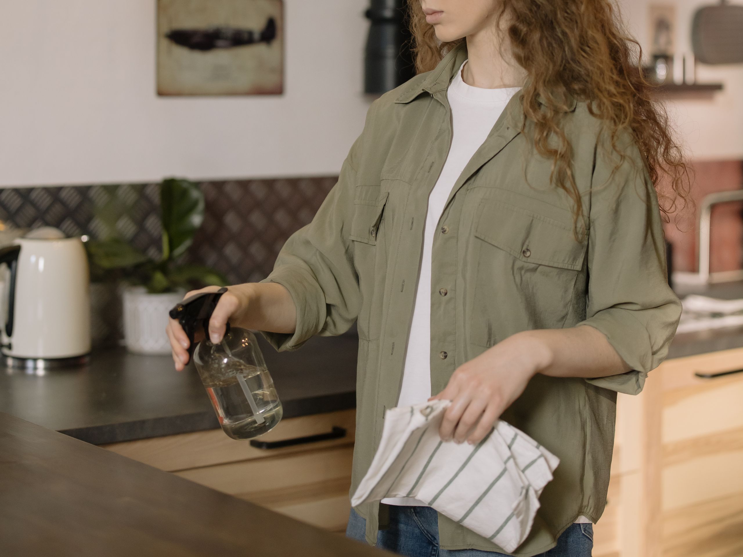 Airbnb Cleaning Schedule: A Simple Routine That Keeps Every Stay Five-Star - A woman with curly hair cleans a kitchen counter using a spray bottle and cloth.