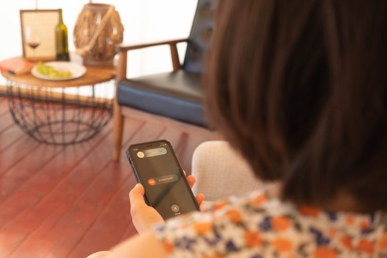 Airbnb Guest Communication: How to Keep Guests Happy Before, During, and After Their Stay - A person using a smartphone's SOS emergency feature indoors with a cozy background.