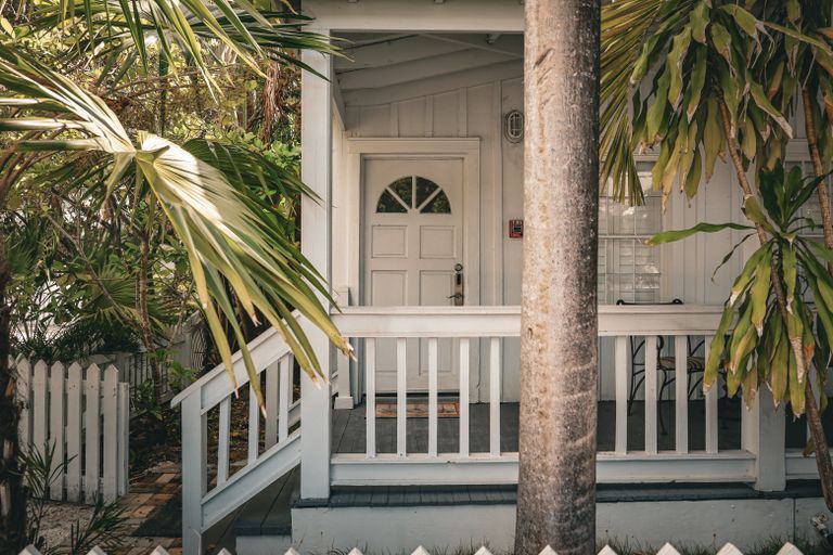 Airbnb House Rules That Protect Your Home Without Scaring Guests Away - Charming tropical front porch with palm trees and white wooden railing, evoking a summer vibe.