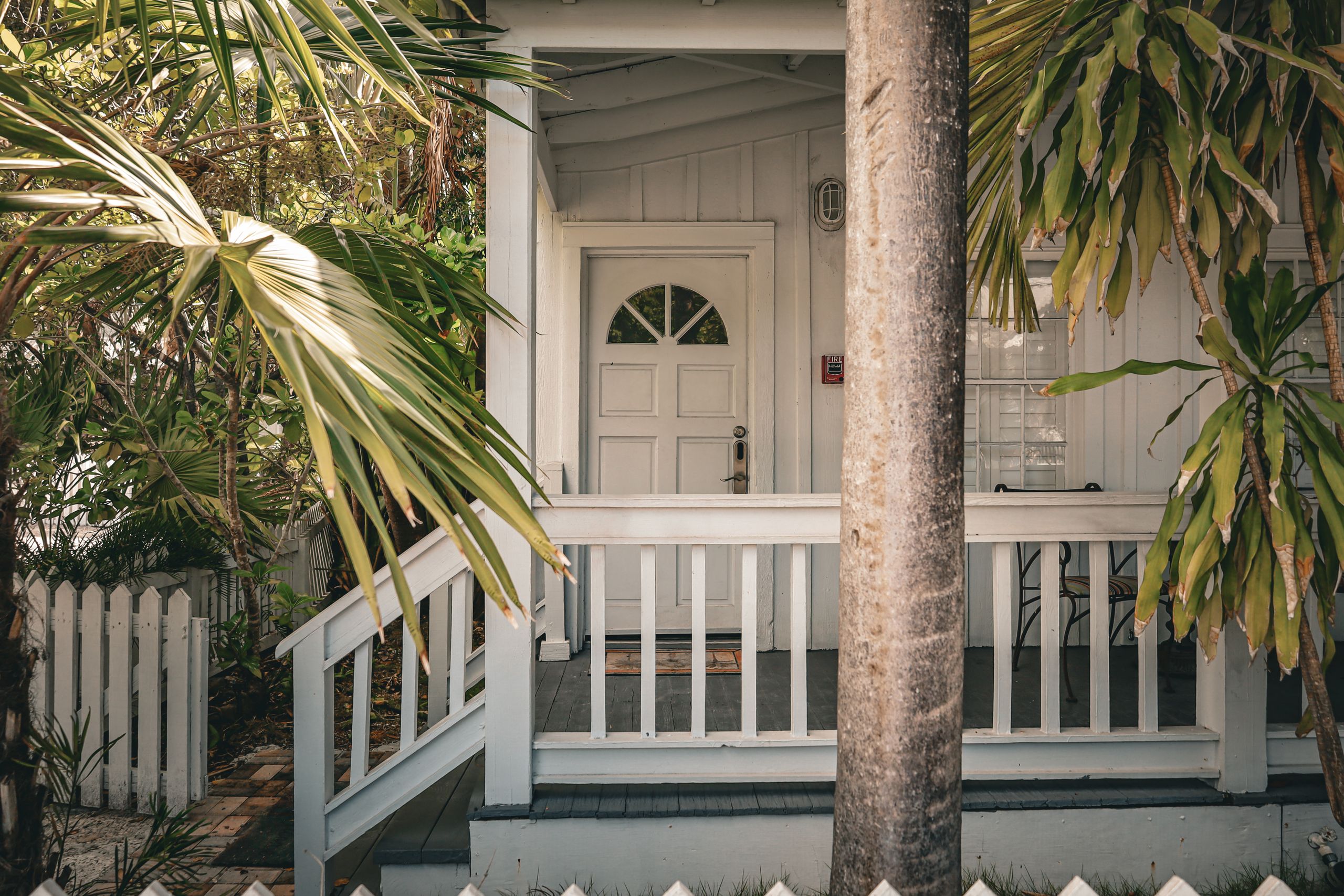 Airbnb House Rules That Protect Your Home Without Scaring Guests Away - Charming tropical front porch with palm trees and white wooden railing, evoking a summer vibe.
