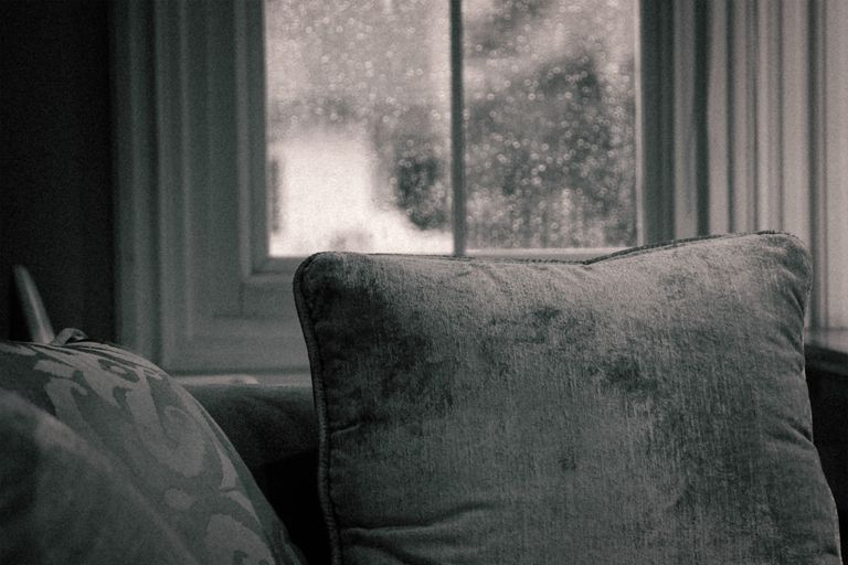 Airbnb Natural Disaster Preparedness: How to Protect Guests and Your Property - A cozy indoor setting with soft pillows by a rainy window, evoking comfort.