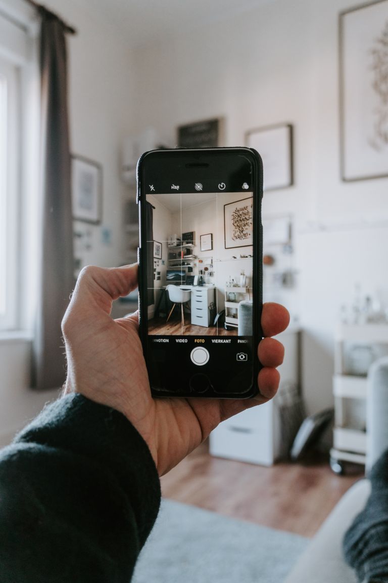 Airbnb Photography Tips: How to Take Listing Photos That Get More Bookings - A hand holding a smartphone capturing a stylish home office setup indoors.