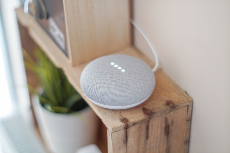 Airbnb Smart Home Devices: The Best Tech Upgrades for Better Guest Experiences - A Google Home Mini smart speaker on a wooden shelf, blending technology with home decor.