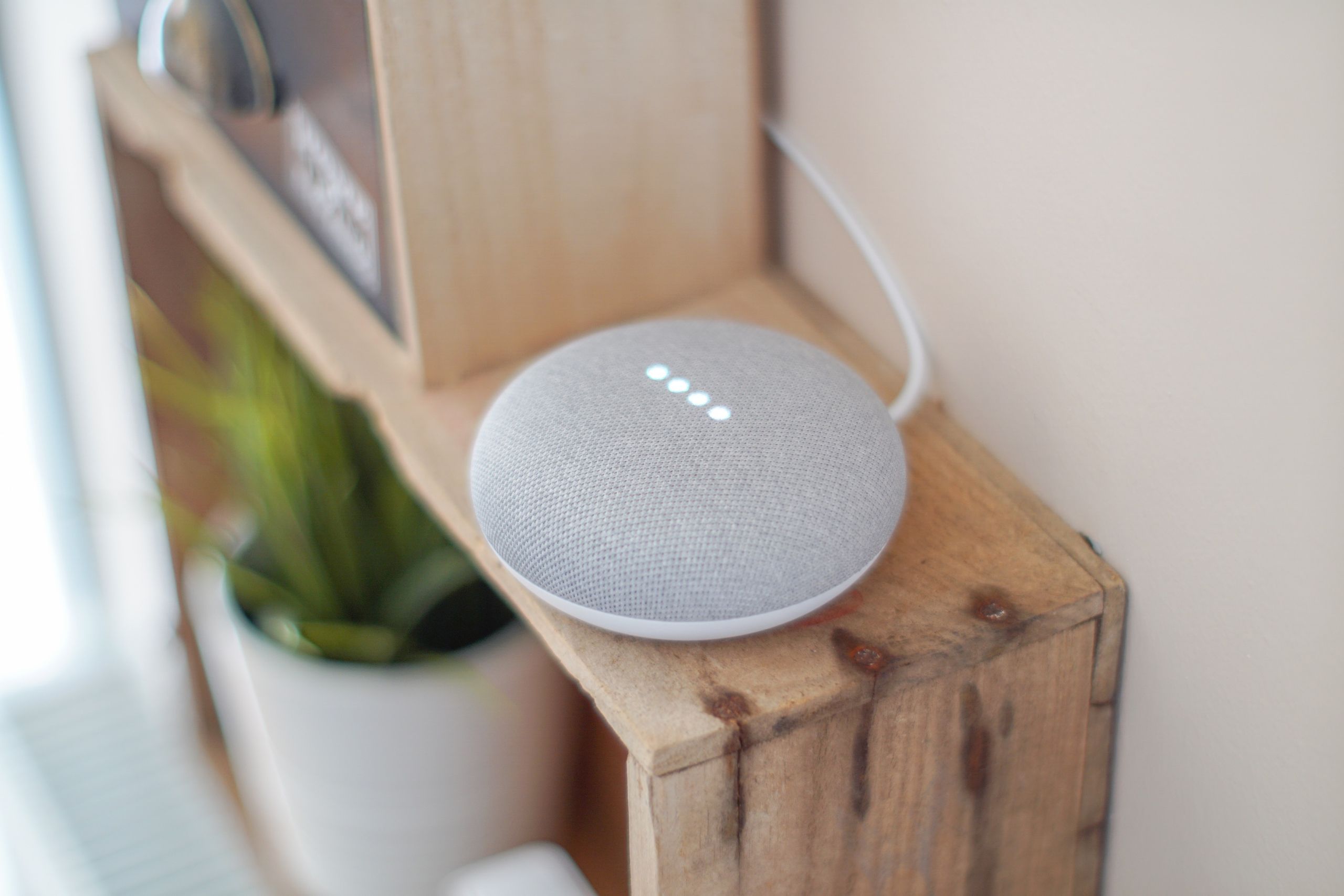 Airbnb Smart Home Devices: The Best Tech Upgrades for Better Guest Experiences - A Google Home Mini smart speaker on a wooden shelf, blending technology with home decor.