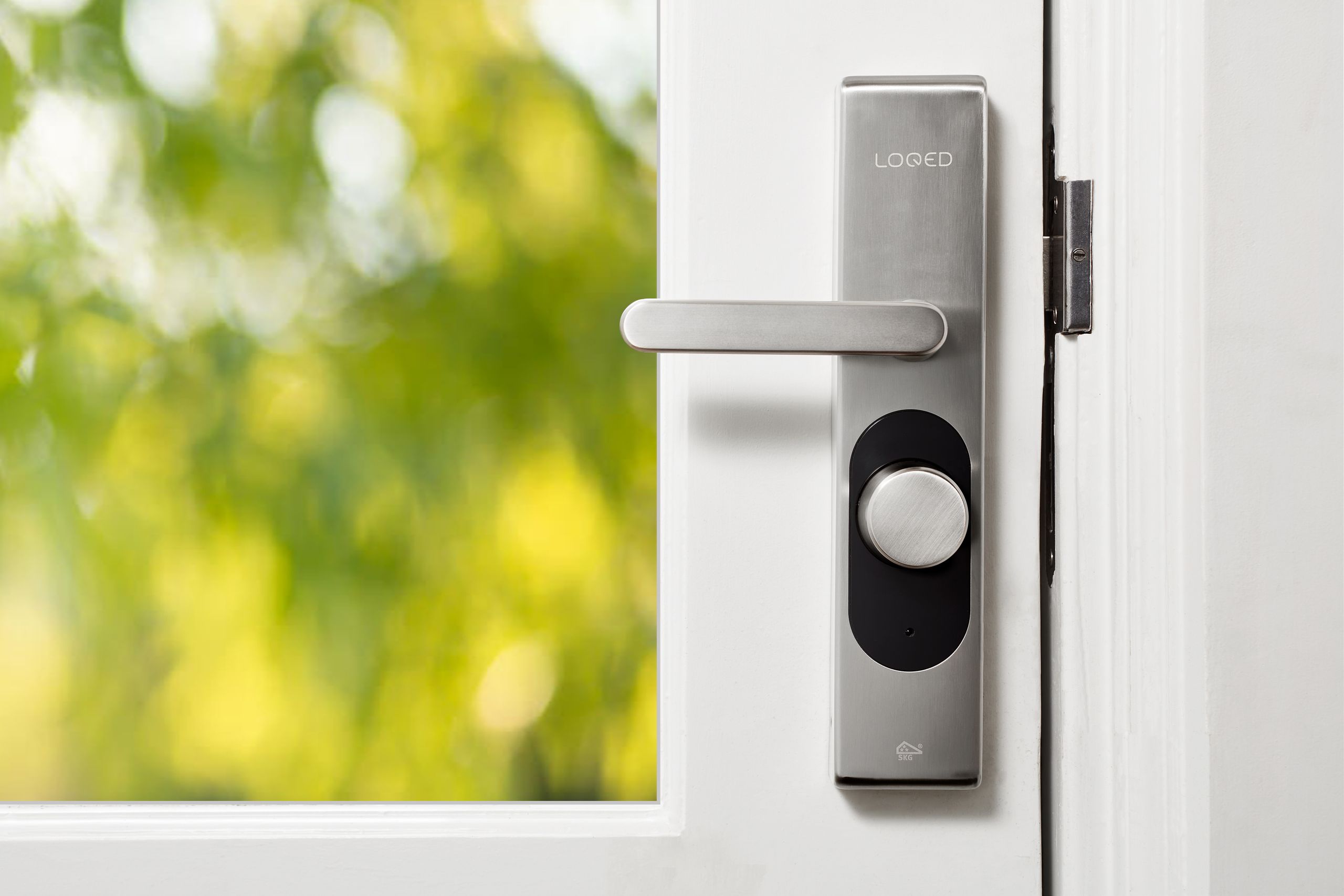 Airbnb Smart Locks: Are They Worth It for New Hosts? - Sleek smart door lock on a white door with blurred green foliage in the background.