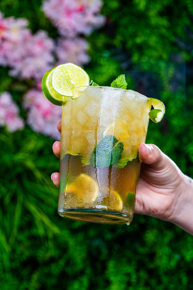 Hand holding a refreshing mint julep cocktail with ice, perfect for summer days.