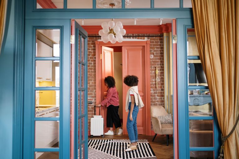 The Art of Hosting Long-Term Airbnb Guests: Tips and Challenges - Stylish room with two women walking through doorway, carrying suitcase. Cozy and colorful decor.