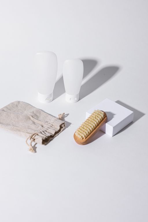 Travel Essentials That Also Work for Airbnb Guests - Elegant display of bathroom accessories including bottles, brush, and cloth on a white background with shadows.