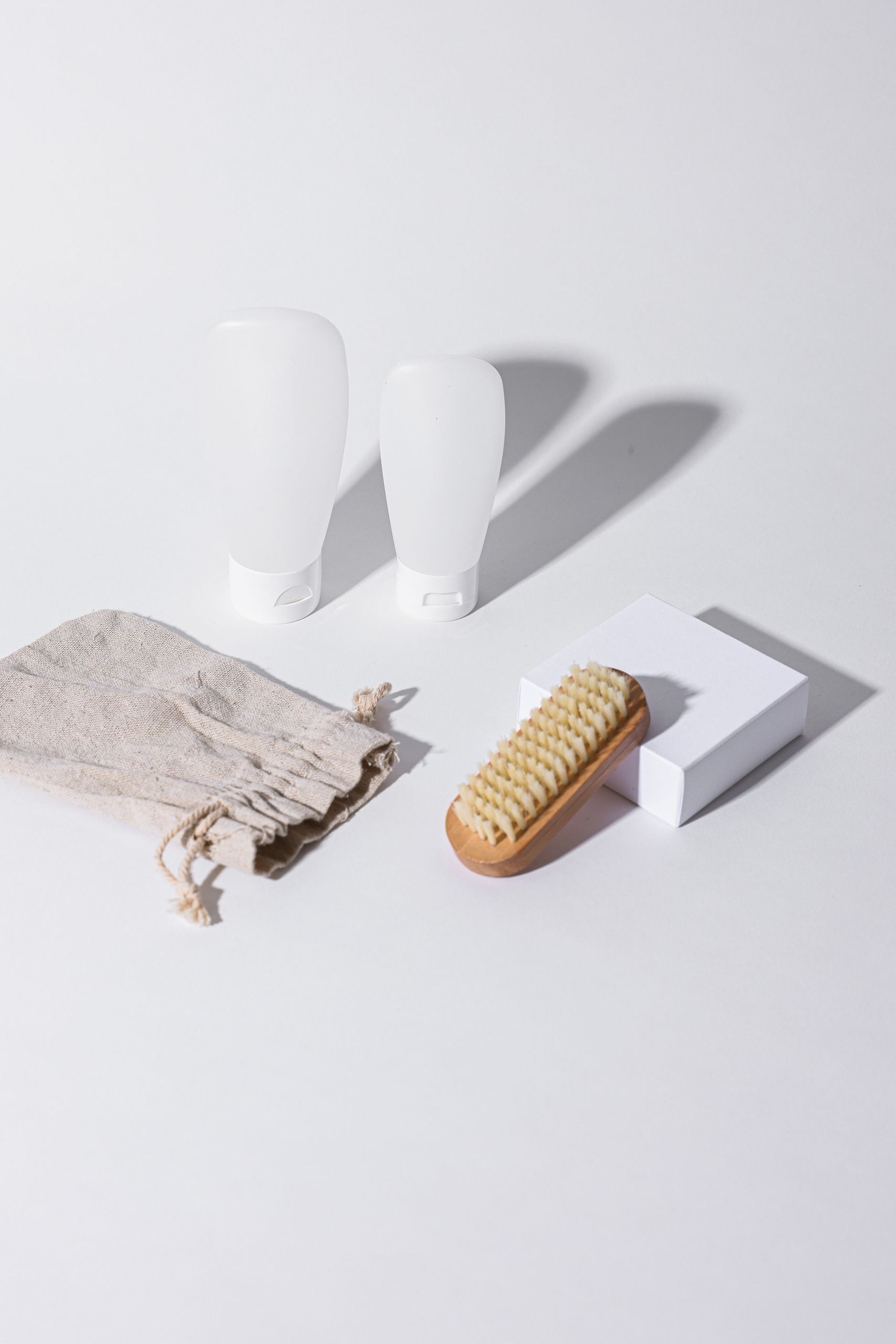 Travel Essentials That Also Work for Airbnb Guests - Elegant display of bathroom accessories including bottles, brush, and cloth on a white background with shadows.