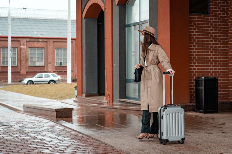 Travel Wellness Essentials for Women Who Stay Ready - Fashionable woman in beige coat and hat with suitcase standing outdoors.