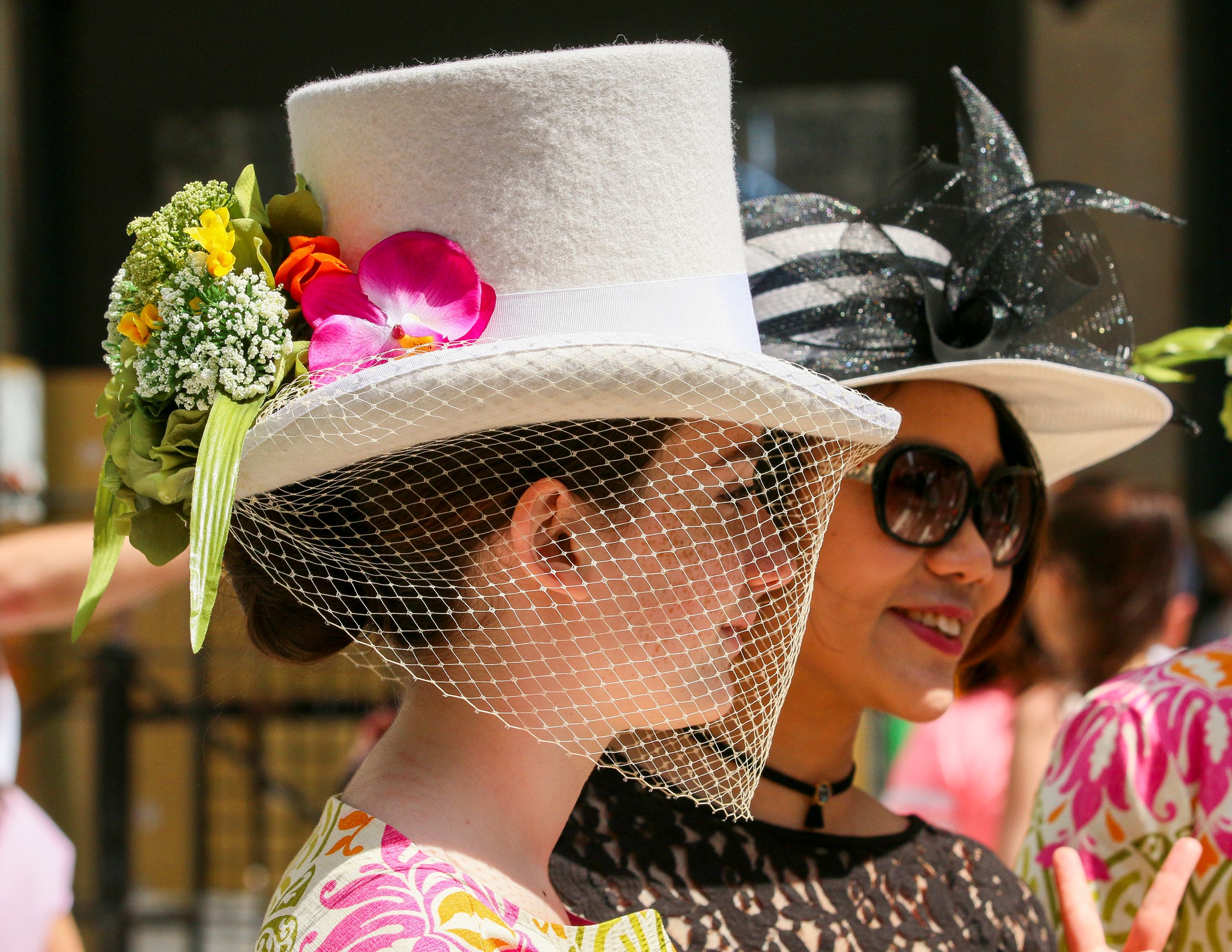 Two women in stylish hats at a fashion parade in New York City.