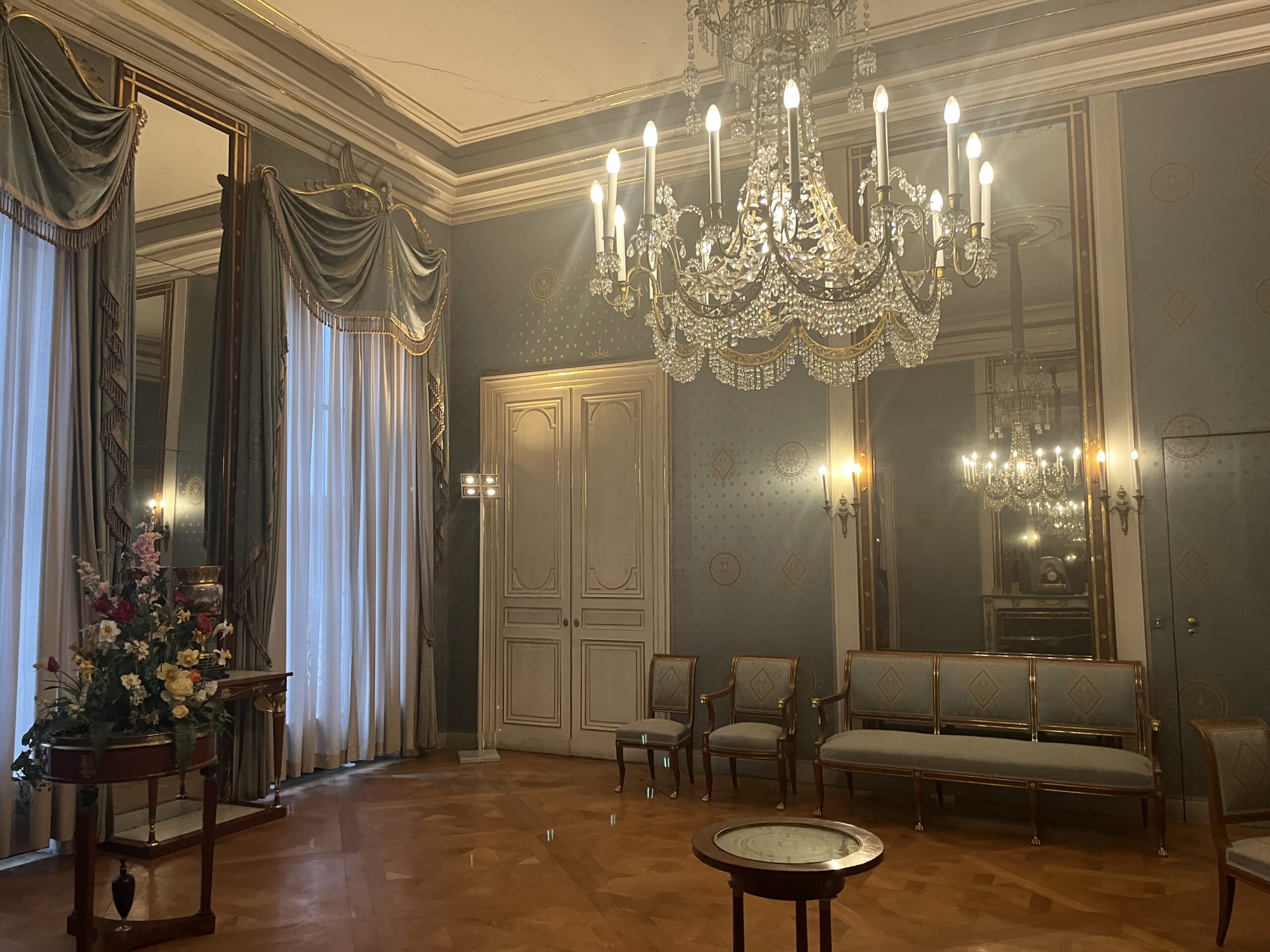Elegant royal room with crystal chandelier, mirrors, blue walls, tall curtains, and gilded furniture at the Munich Residenz
