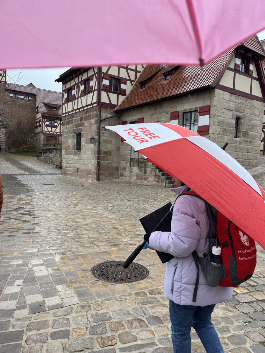 Tour guide carrying a red and white umbrella among historic half-timbered buildings at Nuremberg Imperial Castle