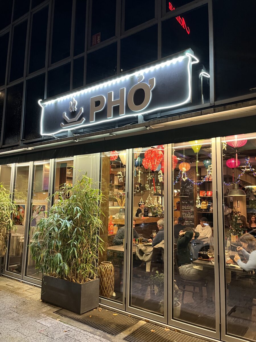 Illuminated PHỞ Vietnamese restaurant storefront decorated with colorful lanterns in Nuremberg