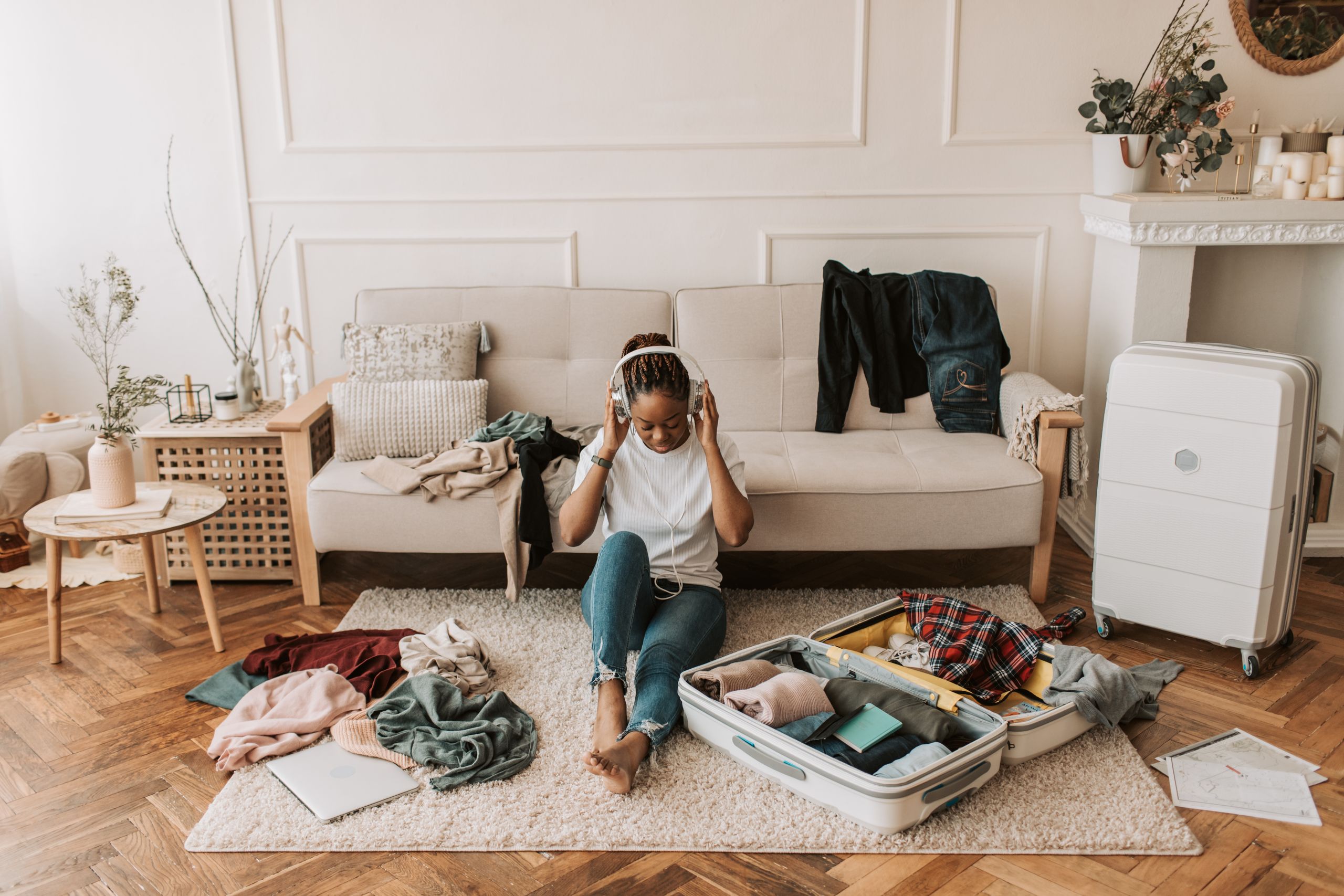 A Good Travel Plan Should Leave Breathing Room - A woman packs a suitcase in her living room while listening to music, surrounded by clothes and a cozy atmosphere.