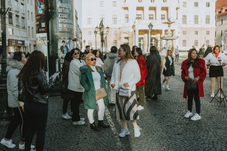 A lively scene of women walking and socializing in Prague's historic Old Town square, capturing urban life and tourism.