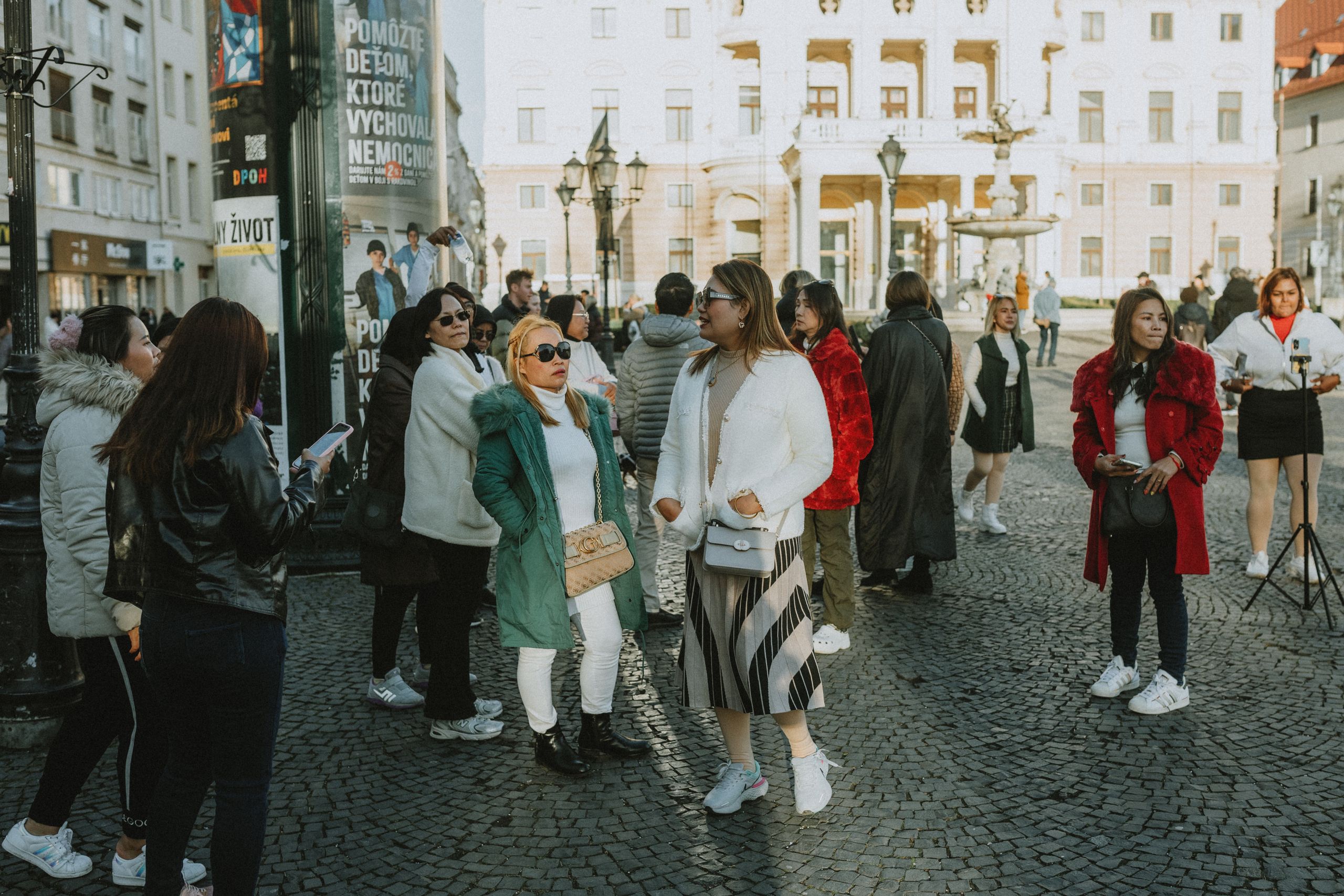 A lively scene of women walking and socializing in Prague's historic Old Town square, capturing urban life and tourism.