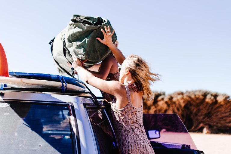 The Freedom Inside a Long Weekend - A woman placing a large bag on a car's roof rack, symbolizing summer travel adventure.