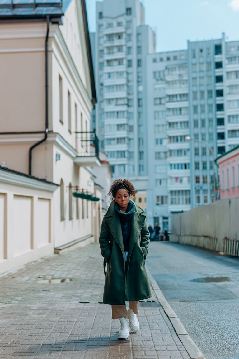 The City Begins at the Corner That Changes My Plan - African American woman in green coat walking on a city sidewalk.