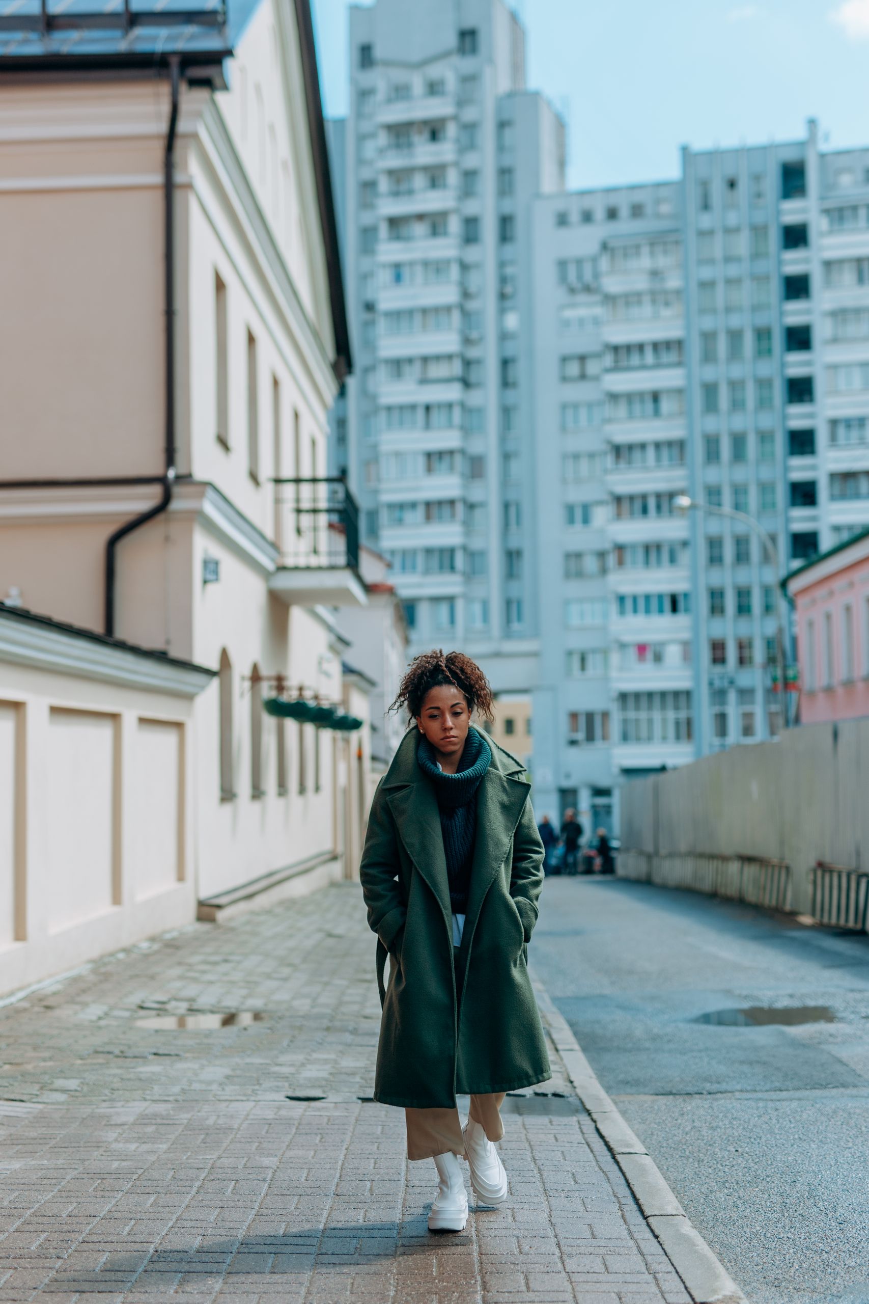 The City Begins at the Corner That Changes My Plan - African American woman in green coat walking on a city sidewalk.